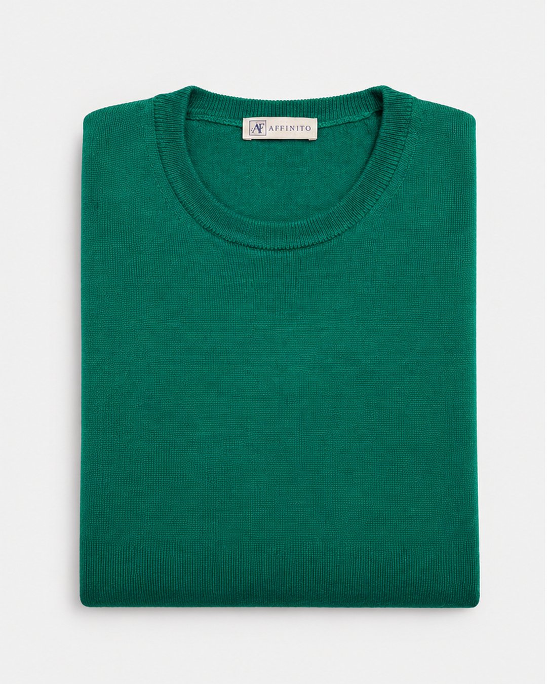 Maglia girocollo in lana merinos verde Affinito, piegata su fondo bianco